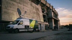 Übertragungswagen mit Satellitenschüssel steht neben einem beleuchteten Fußballstadion